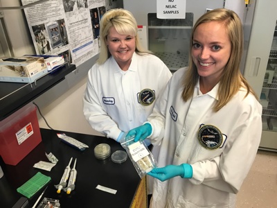 Sarah Wallace (L), NASA microbiologist and Genes in Space-3 principal investigator, and Sarah Stahl (R), microbiologist, are seen in their Johnson Space Center lab with the in-flight sample from the Genes in Space-3 investigation